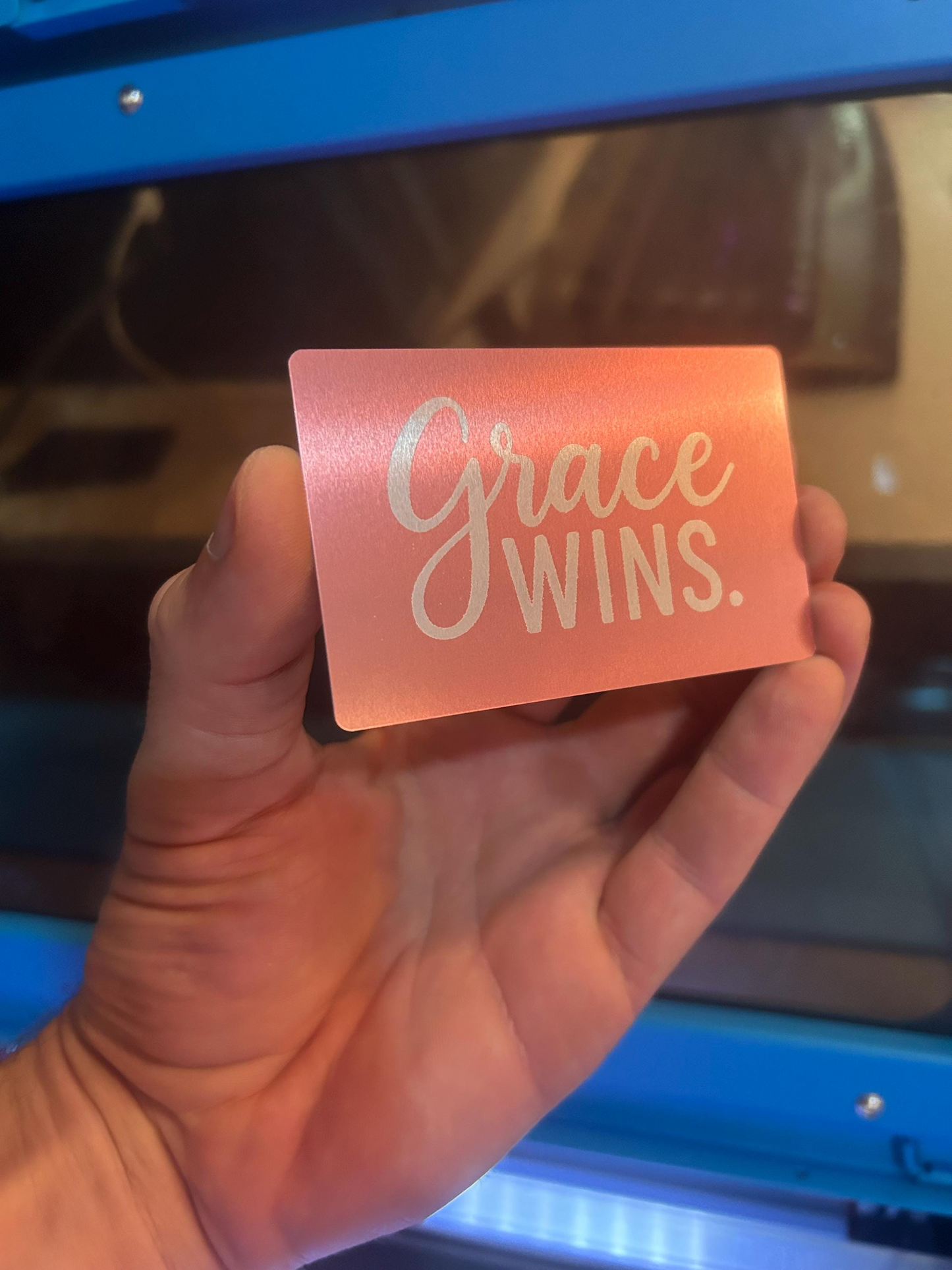 Hand holding a pink card with inspirational 'Grace Wins' typography design text in front of a blue background