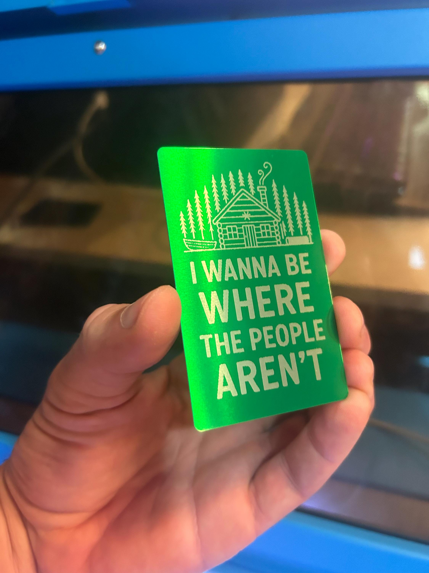 Hand holding a green card with text and a cabin illustration, set against a blurred indoor background.