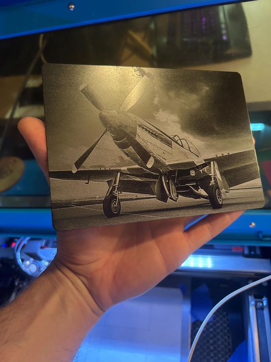 Hand holding a laser engraved black/silver highly detailed aircraft enthusiast engraving in front of a blue machine background