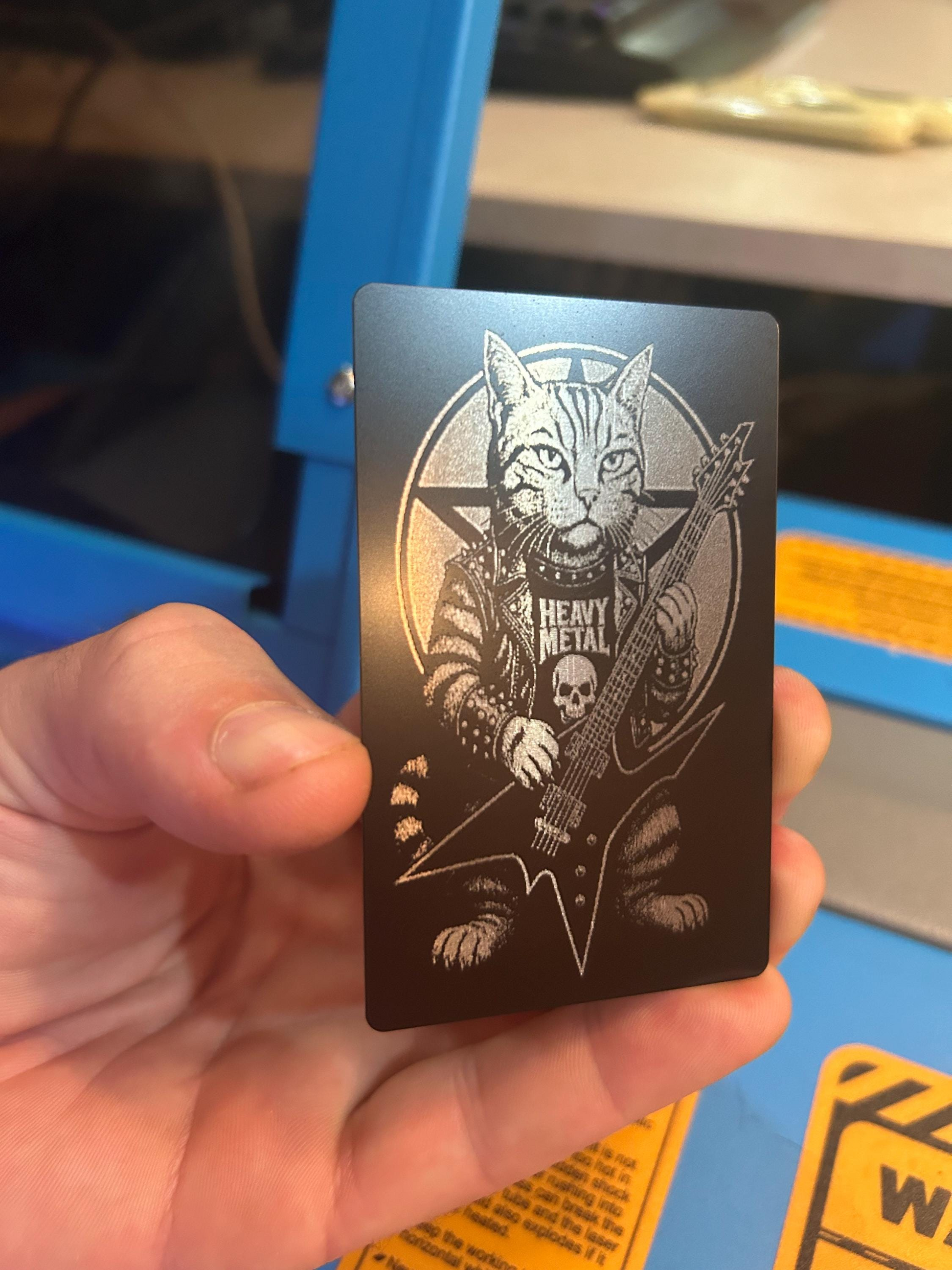 Hand holding a metallic card with a cat playing guitar and 'Heavy Metal' illustration.