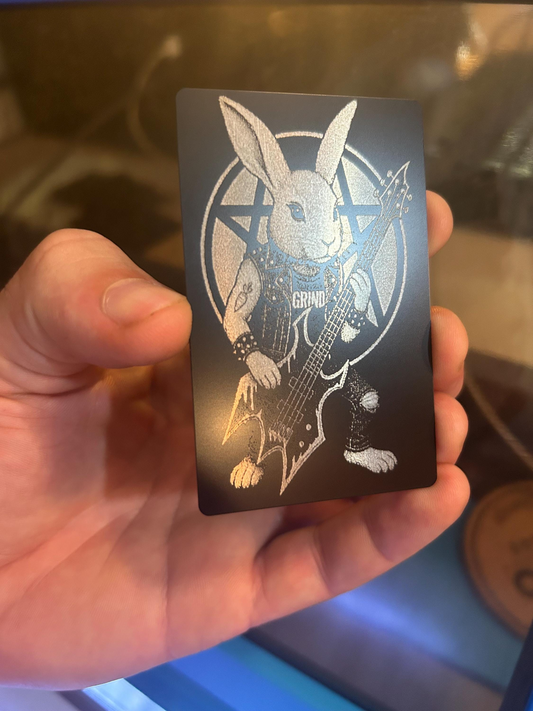 Hand holding a laser engraved metal business card with a rabbit playing guitar design on a dark background