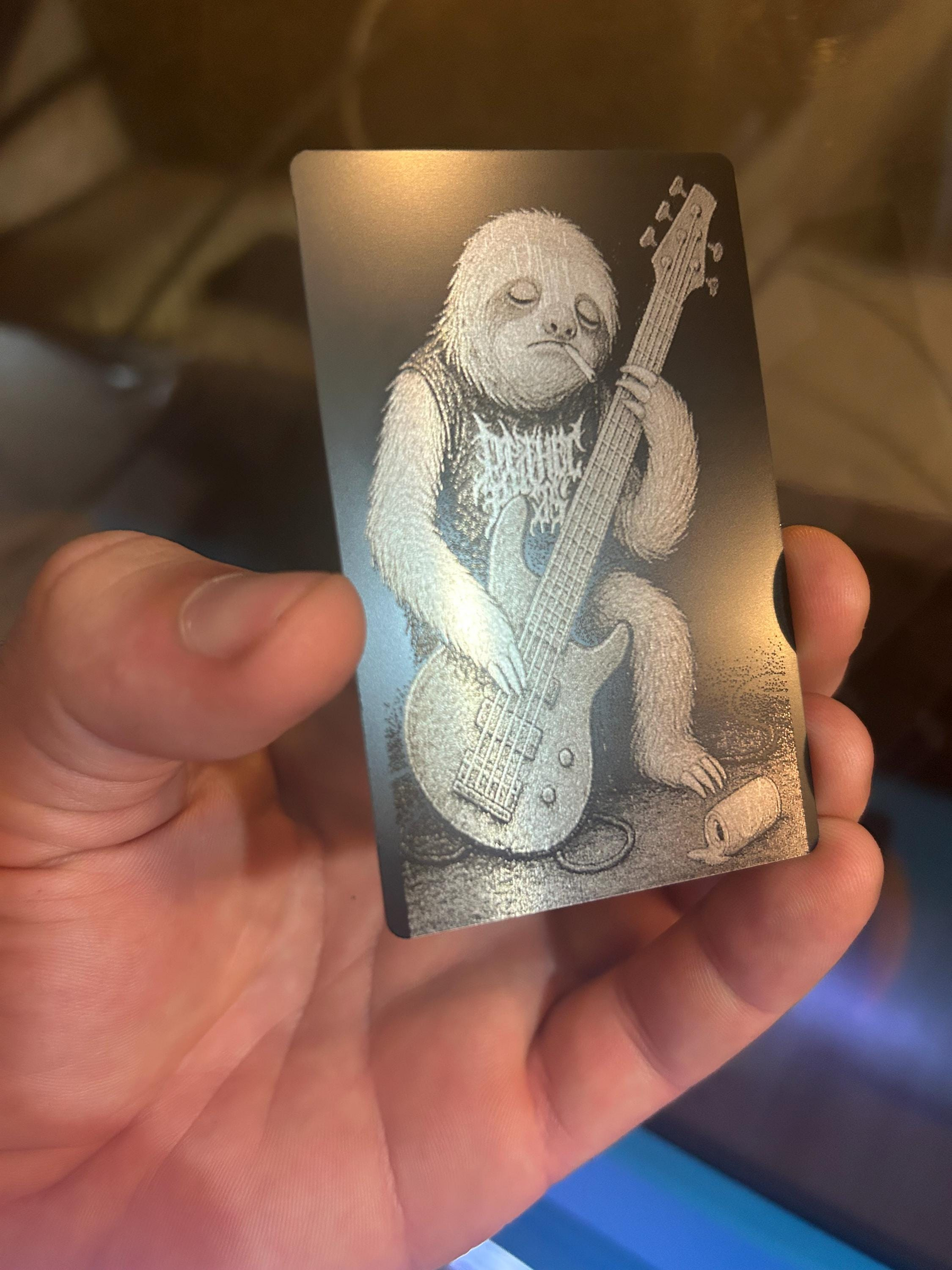 Hand holding a laser engraved anodized aluminum gift card with a cartoon sloth playing a guitar illustration, funny gift for musicians