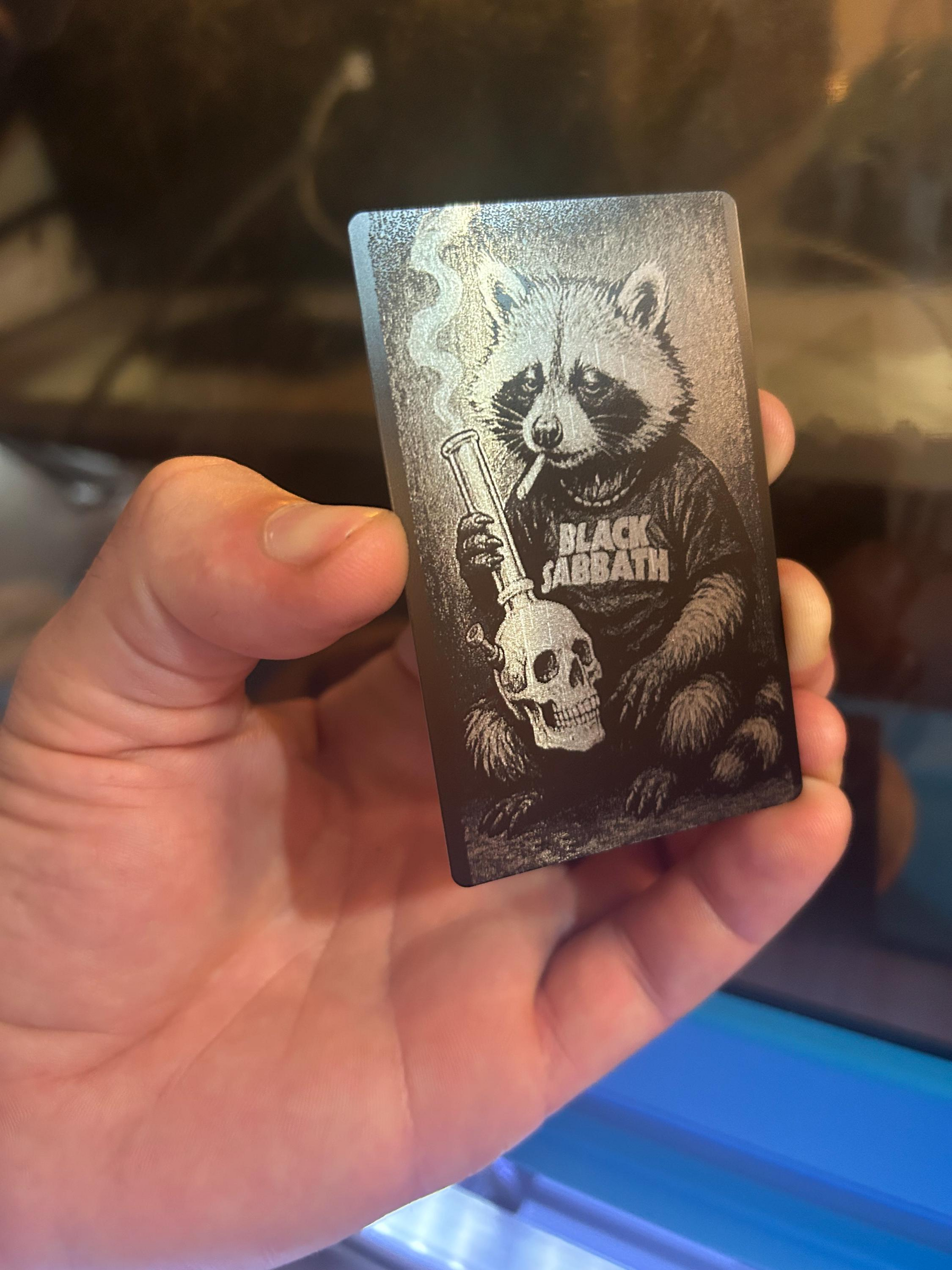 Hand holding a highly detailed laser engraved illustration novelty art of black and silver raccoon hipster music gag gift card