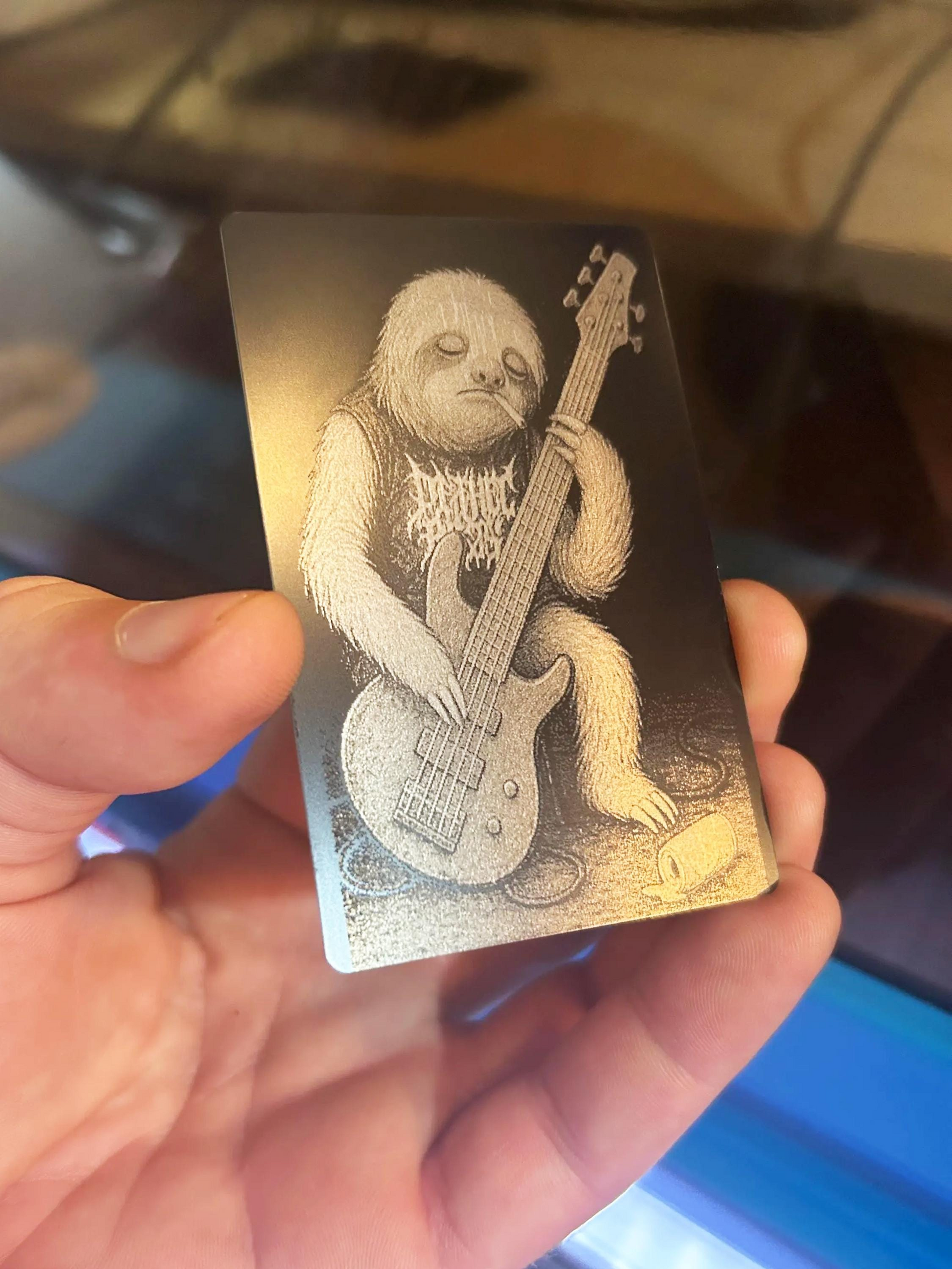 Hand holding a metal business card with a bear playing a bass guitar illustration.