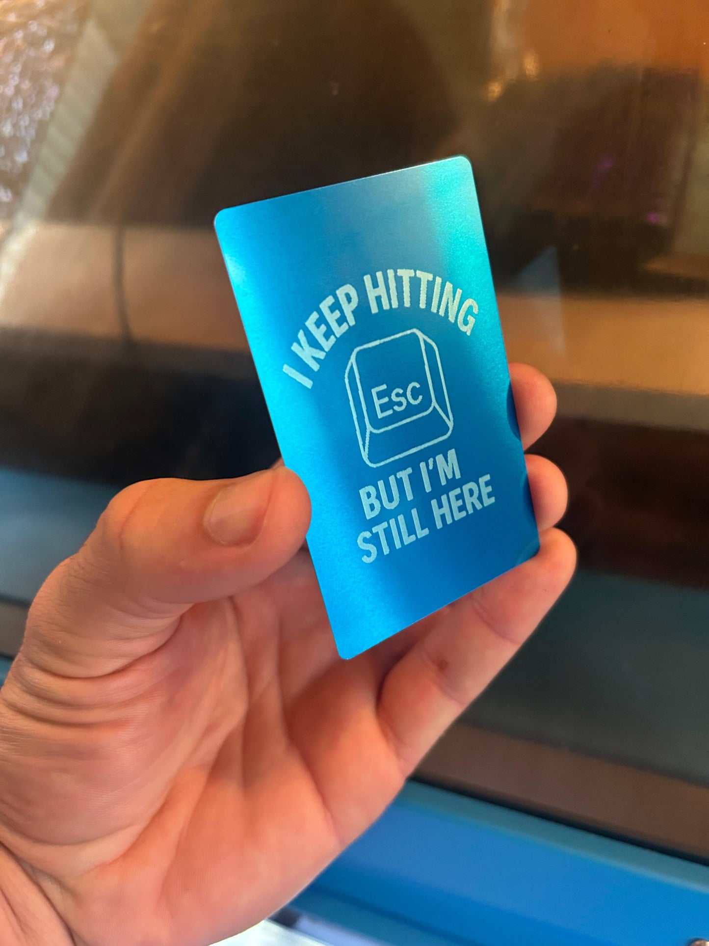 A funny laser engraved metal keepsake card that reads "I Keep Hitting Escape But I'm Still Here" with a picture of an Esc keyboard key in blue/silver anodized aluminum