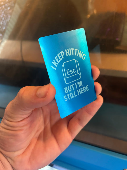 A funny laser engraved metal keepsake card that reads "I Keep Hitting Escape But I'm Still Here" with a picture of an Esc keyboard key in blue/silver anodized aluminum