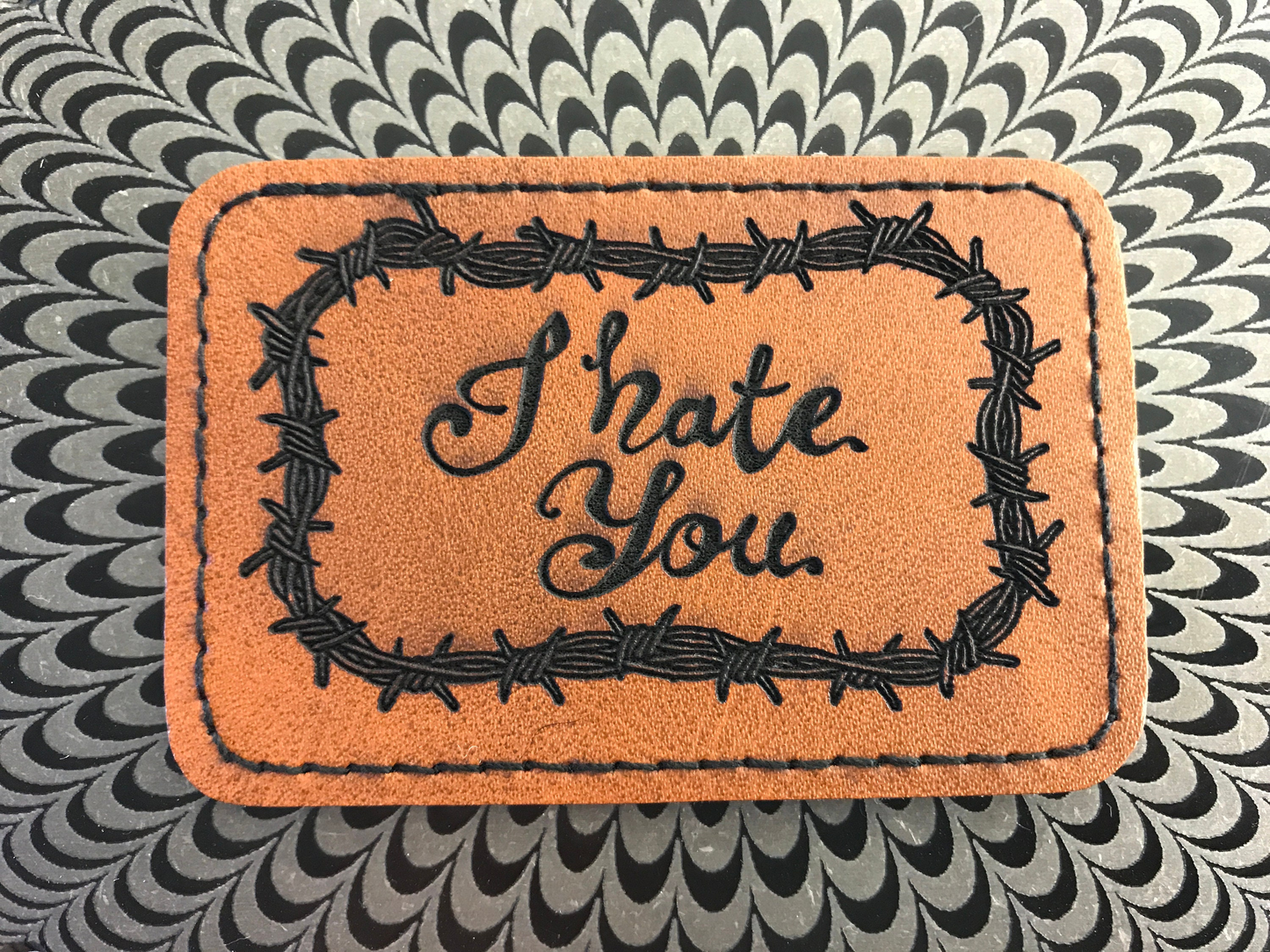 Brown leather Patch with 'I Hate You' text and barbed wire design on a patterned background