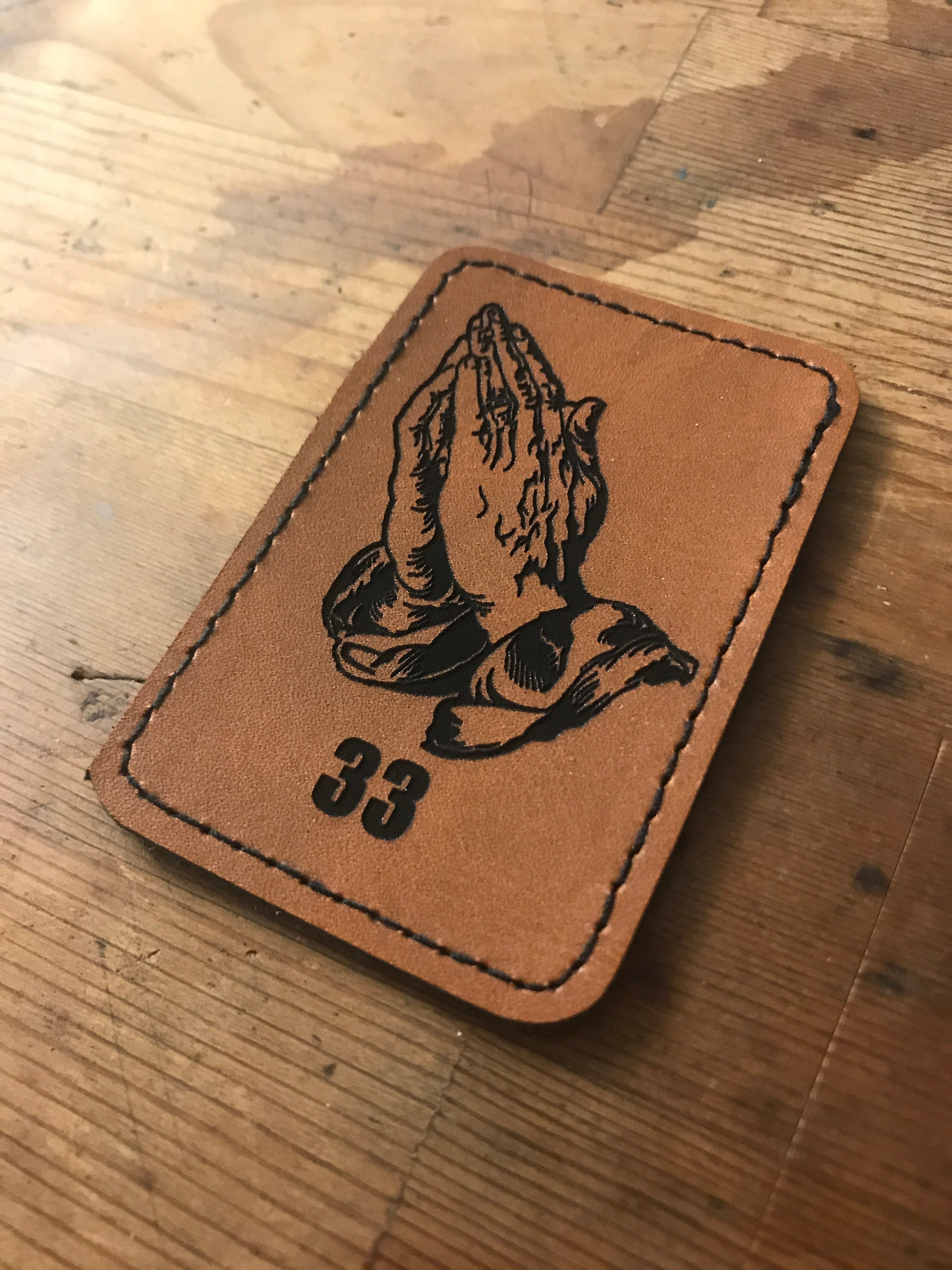 Brown leather patch with praying hands and number 33 on a wooden surface