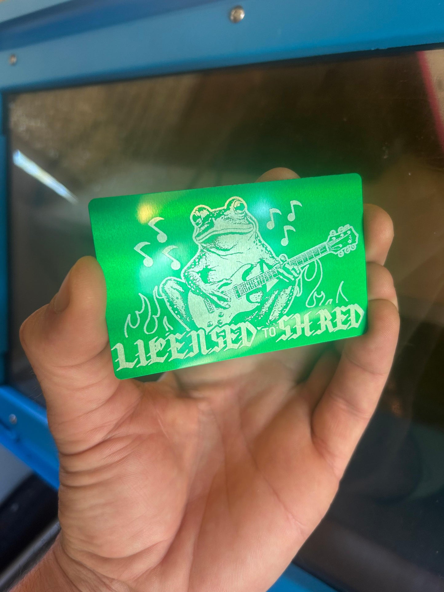 Laser engraving with License to Shred design, with a frog playing guitar in green/silver