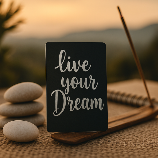 Black mini placard with 'live your dream' text on a wooden stand with stones and notebook in the background.