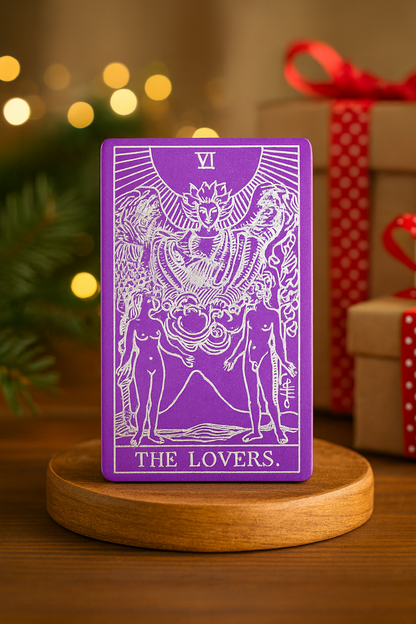 Purple/silver metal tarot card titled 'The Lovers' on a wooden stand with festive background