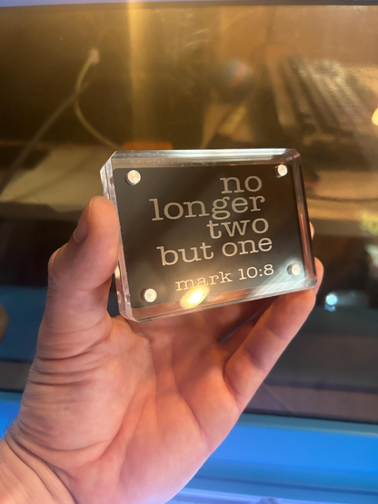 Hand holding a clear acrylic block with engraved text against a blurred background