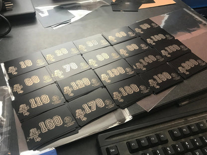 Stacks of bulk laser engraved metal business cards with custom text and design, pictured on a work desk