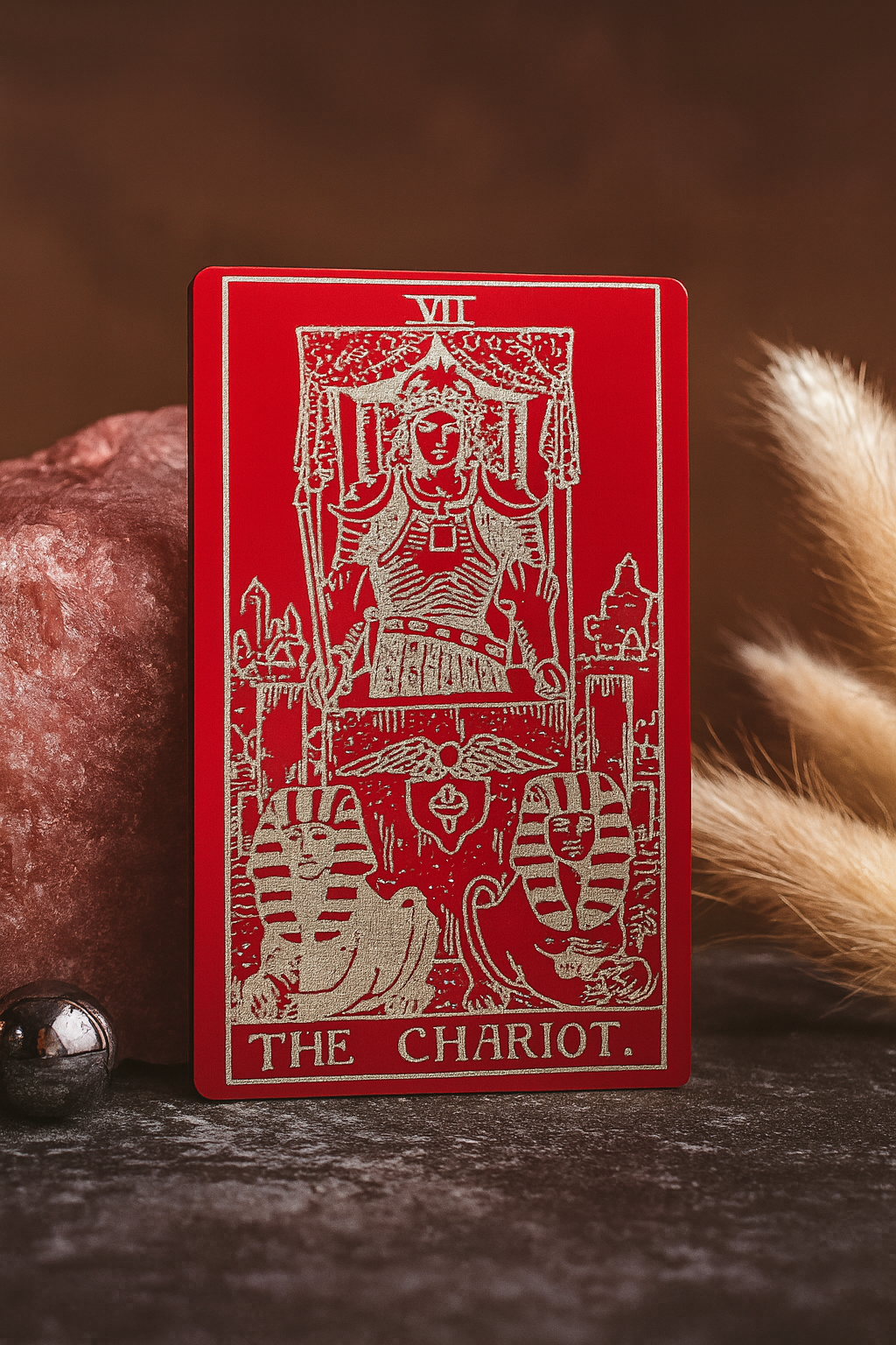 Red/silver metal tarot card titled 'The Chariot' with intricate designs on a dark background.