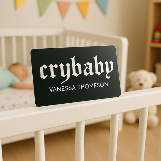 Black sign with 'crybaby' and 'Custom Name' text on a crib in a nursery.