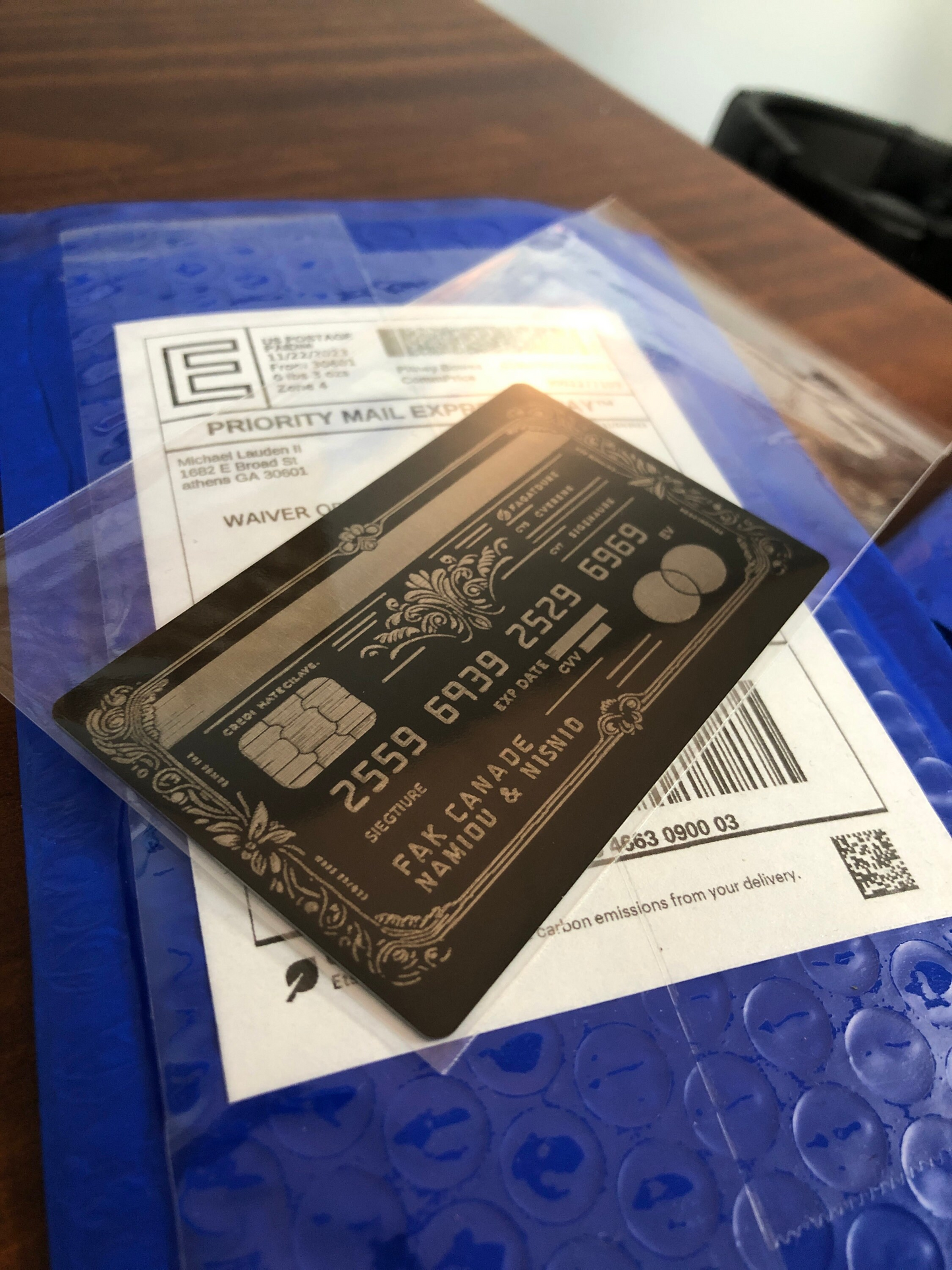 Black and silver laser engraved faux credit card with gold details on a Priority Mail envelope