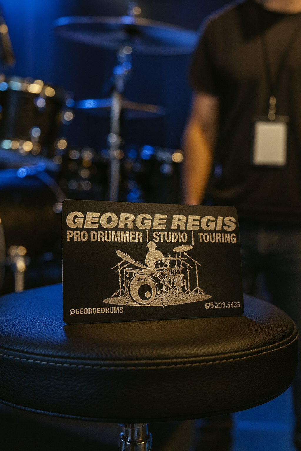 Personalized Metal Business card for George Regis, Pro Drummer, Studio, Touring, on a drum stool with a blurred drum set in the background.