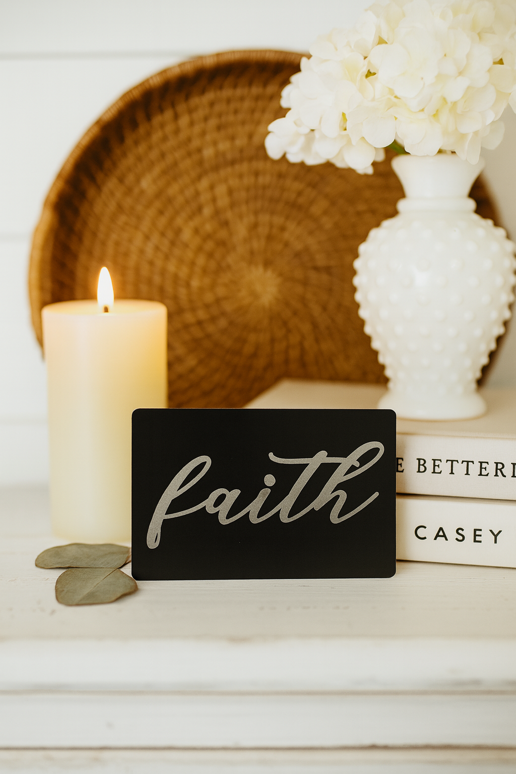 Decorative metal sign with 'faith' on a shelf with a candle and vase.