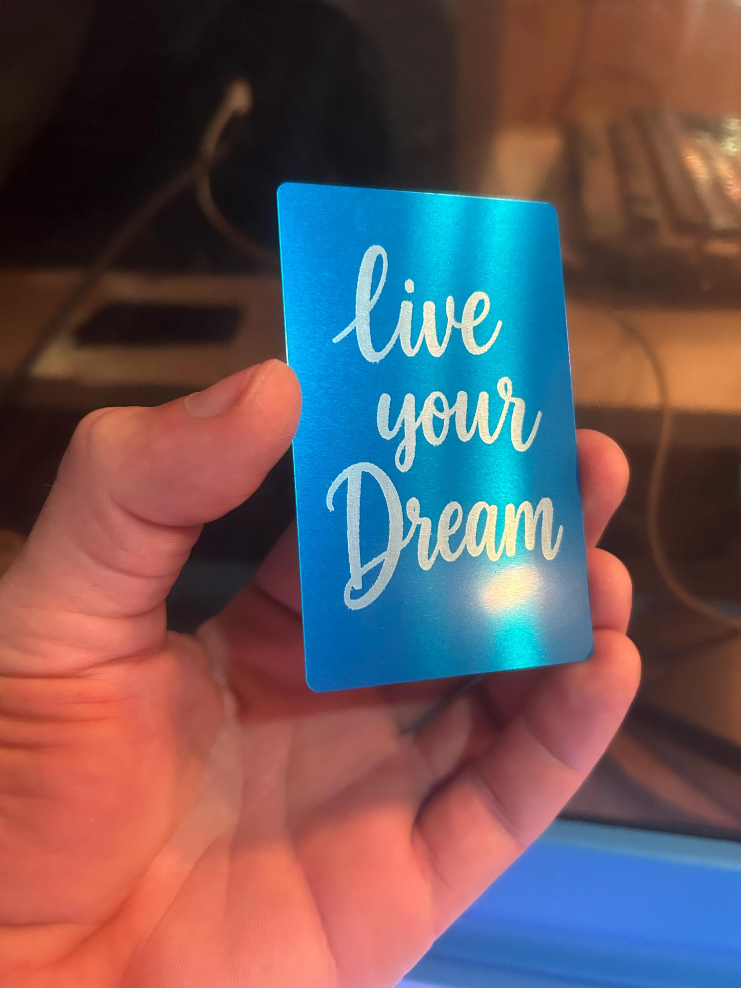 Angled shot of custom engraved metal keepsake card – “Live Your Dream” typography design in silver on blue