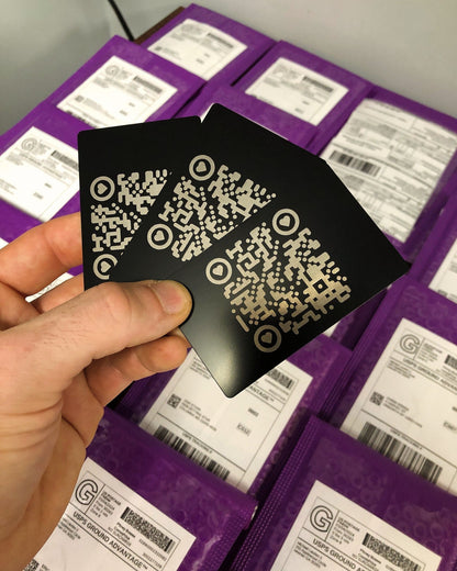 A hand holding three black anodized aluminum QR code cards with a matte finish, capable of being personalized with engraved text.