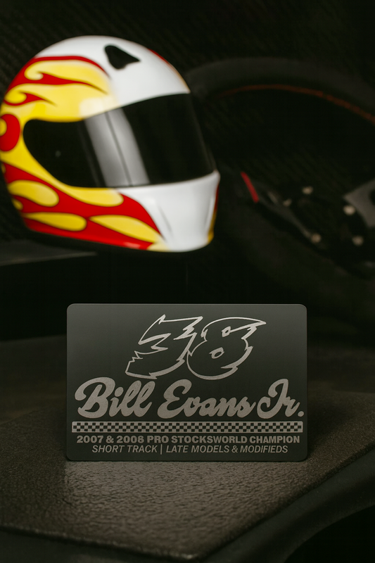 Race car driver helmet with flames and a laser engraved metal business card with personalized text on a dark background
