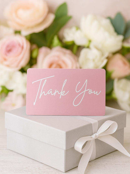 Pink 'Thank You' card on a white box with flowers in the background
