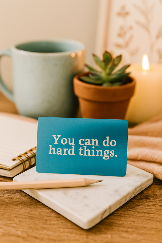 Anodized aluminum motivational card with 'You can do hard things' on a desk with a mug, plant, and candle.