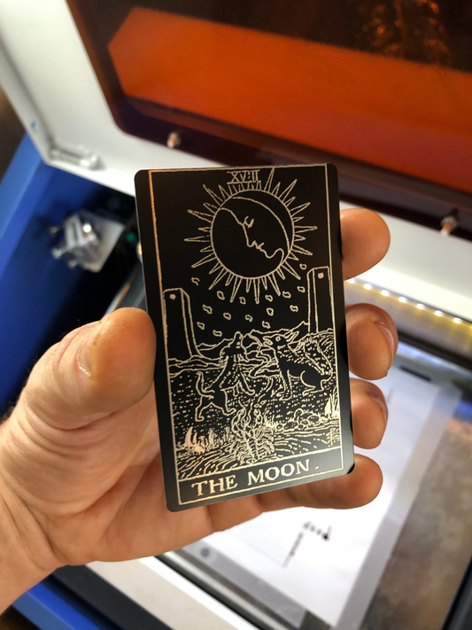 Hand holding a black metal tarot gift card with 'The Moon' symbol and text.