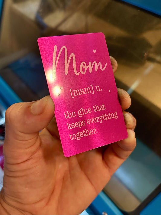 A hand holding a bright metal purple card with laser engraved silver text that reads 'Mom [mam] n. the glue that keeps everything together.