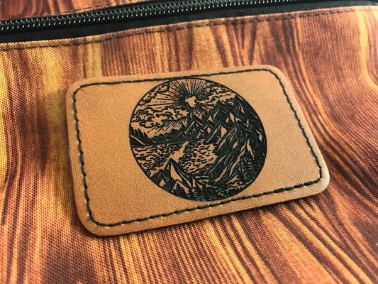 Patch with geometric nature mountain design on a brown leather patch on a front pocket of a backpack with wood grain pattern