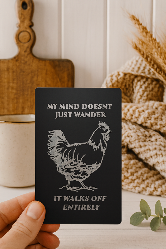 Black card with a rooster illustration and humorous text held by a hand, with a rustic background.