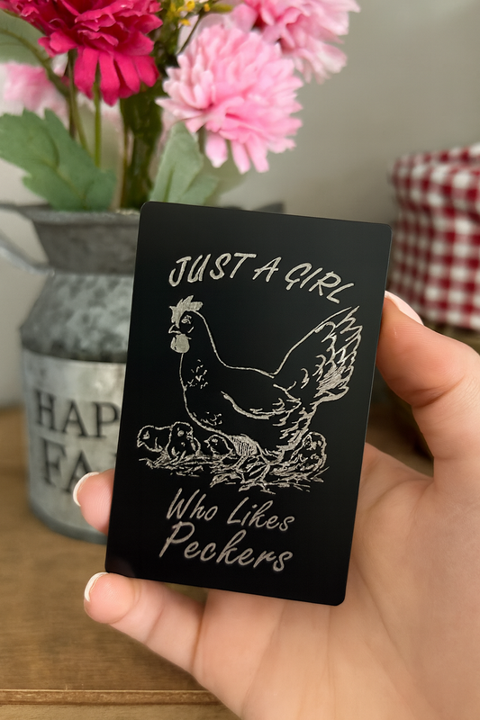 Hand holding a laser engraved metal gag gift card with chicken and chicks illustration that reads "Just a girl who likes peckers" funny gifts for her