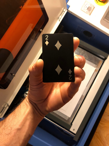 Hand holding a metal two of diamonds playing card with a machine in the background