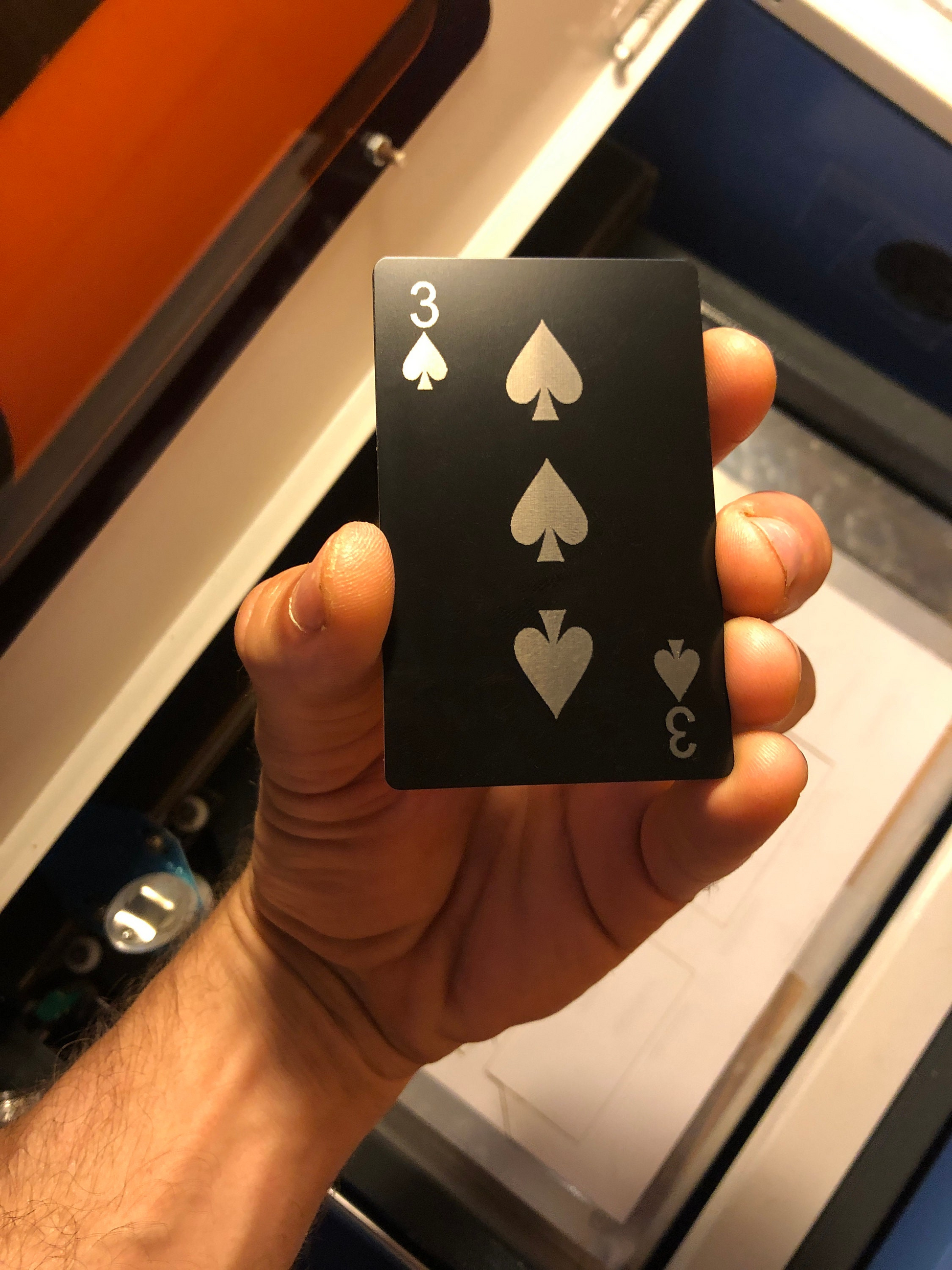 Hand holding a metal poker card with three of spades laser engraving design in black/silver