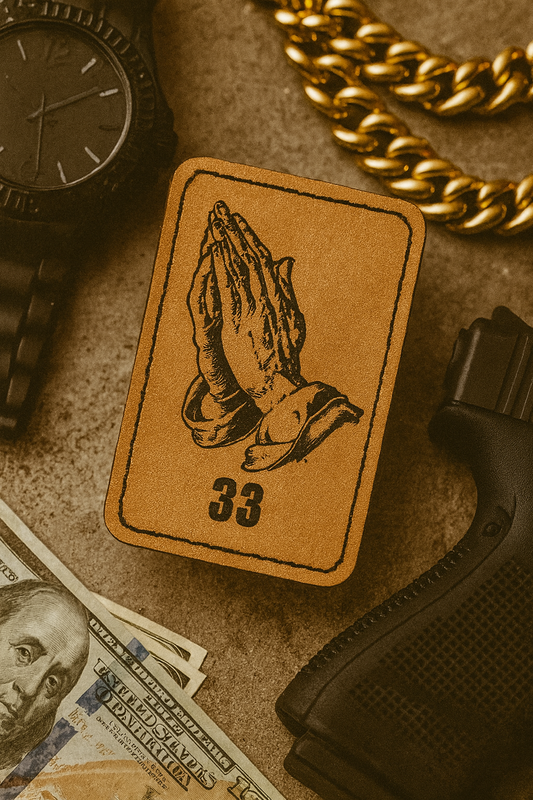 Leather patch with praying hands design, watch, gold chain, and gun on a textured surface.