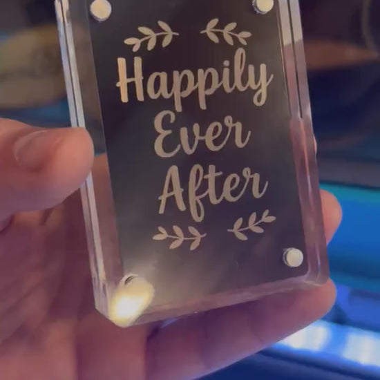 Hand holding laser engraved metal couples keepsake card that reads "Happily Ever After" typography art in black/silver anodized aluminum