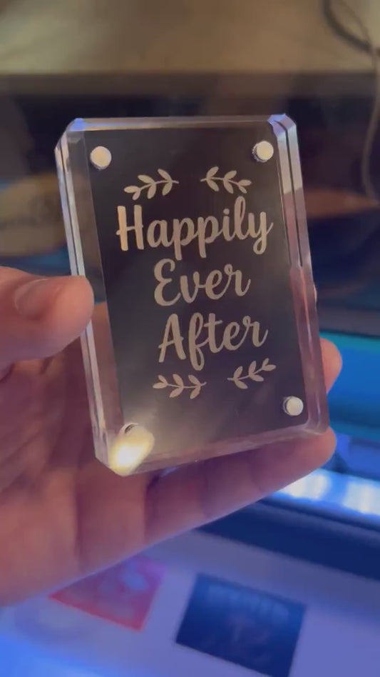 Hand holding laser engraved metal couples keepsake card that reads "Happily Ever After" typography art in black/silver anodized aluminum