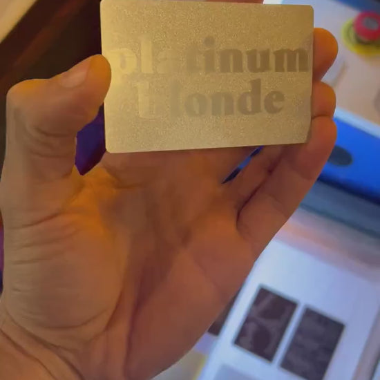 Engraved metal business card turning under light to highlight platinum blonde typographic design and reflective surface