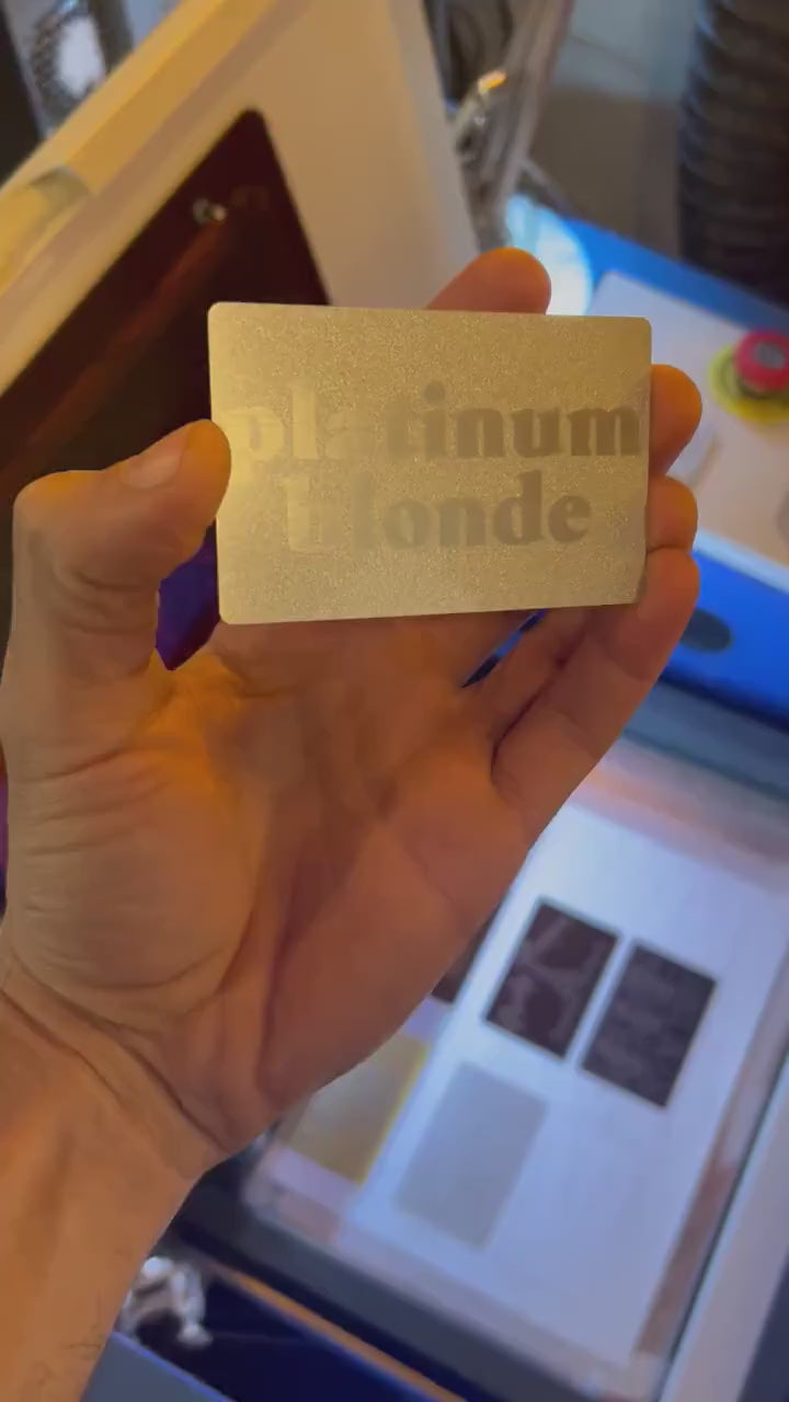 Engraved metal business card turning under light to highlight platinum blonde typographic design and reflective surface