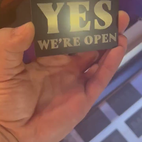 Video of a hand holding a laser engraved "Yes We're Open" / "No We're Closed" metal mini signage placard