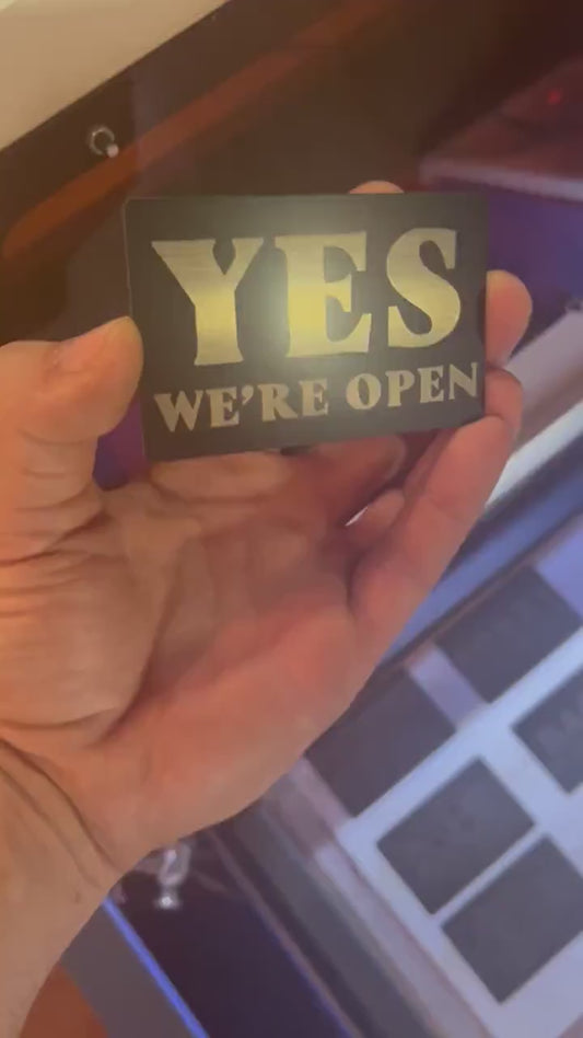 Video of a hand holding a laser engraved "Yes We're Open" / "No We're Closed" metal mini signage placard