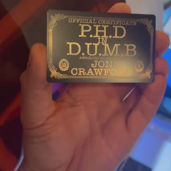 Close-up video of black anodized metal card with PHD in DUMB funny custom text rotating to show laser engraved design