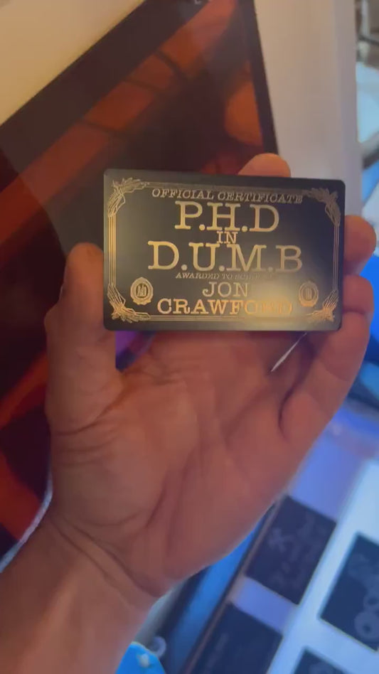 Close-up video of black anodized metal card with PHD in DUMB funny custom text rotating to show laser engraved design