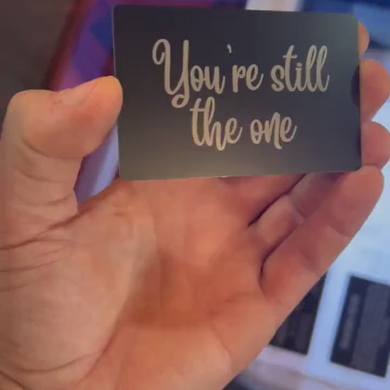 Video of a hand holding a romantic keepsake laser engraved gift card that reads: "You're Still The One", rotating in light to demonstrate reflective properties
