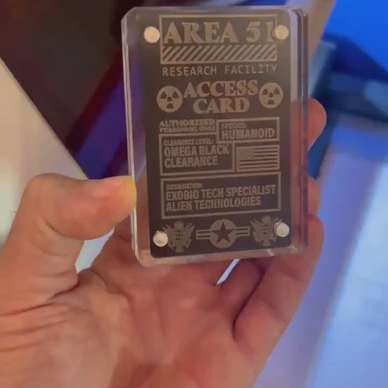 Close up video of hand holding a laser engraved metal gift card with Area 51 Access Card gag top secret text and artwork design, shown in optional acrylic display case