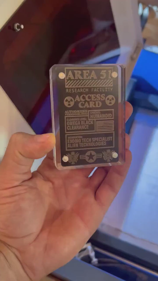 Close up video of hand holding a laser engraved metal gift card with Area 51 Access Card gag top secret text and artwork design, shown in optional acrylic display case