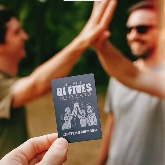 Hand holding a metal hi five club card while two people high five in background
