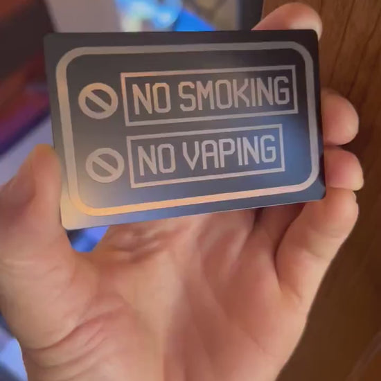 Close up video of hand holding a laser engraved metal placard with No Smoking, No Vaping graphic