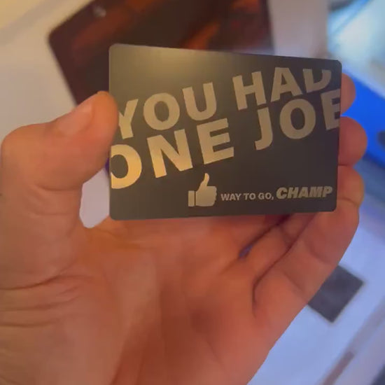 Custom anodized aluminum card being rotated to highlight engraving design for "you had one job, way to go champ" metal gift card