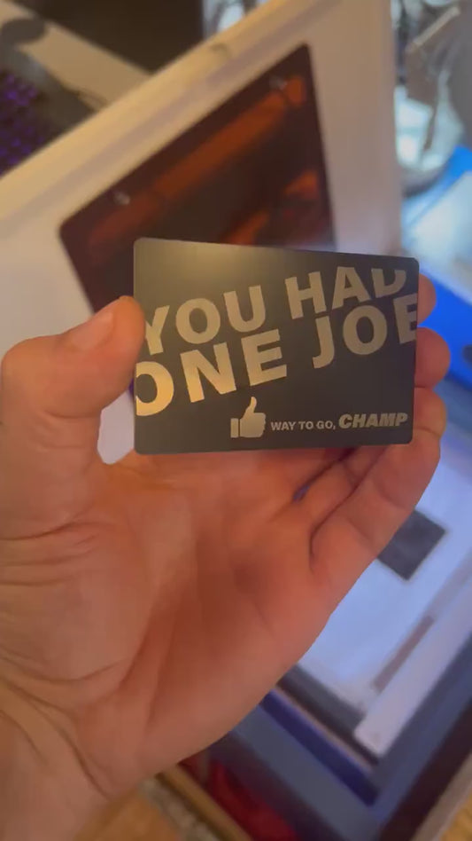 Custom anodized aluminum card being rotated to highlight engraving design for "you had one job, way to go champ" metal gift card